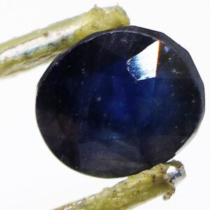 Close-up of a sparkling loose sapphire held with tweezers.