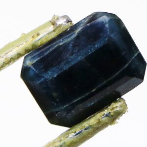 Loose blue Neelam gemstone held in tweezers, showcasing its depth.