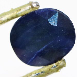 Loose navy blue sapphire gemstone held in tweezers, showcasing its richness.