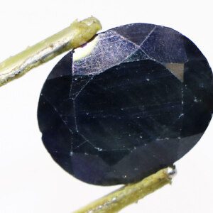 Close-up of a vibrant Neelam Ratna (sapphire) held in tweezers.