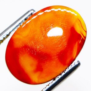 Close-up photo of an Orange Botswana Agate loose gemstone held in tweezers, showcasing its vibrant orange color and unique patterns.