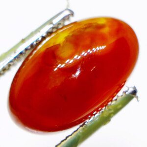 Close-up photo of a natural agate crystal held in tweezers, showcasing its vibrant color and unique banding.