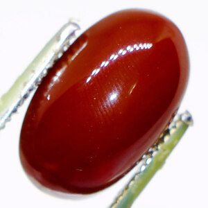 Close-up of Akik agate loose gemstone held in tweezers, showcasing its natural color and pattern.