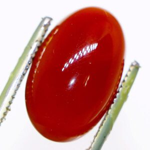 Close-up of a Yemeni agate loose gemstone held in tweezers, showcasing its vibrant color and unique inclusions.