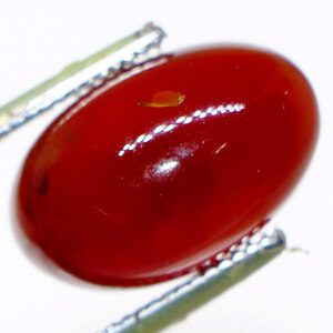 Close-up of a loose agate gemstone held in tweezers, showcasing its vibrant color and banding.