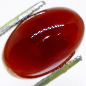 Vibrant Carnelian Aqeeq stone held in tweezers, glowing under light