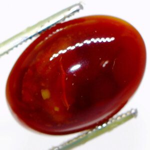 Certified Red Hakik stone held in tweezers, glowing in natural light