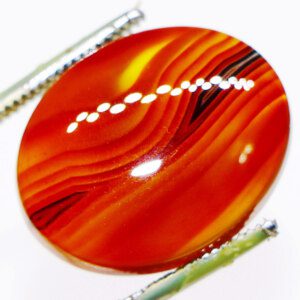 Closeup photo of Aqeeq Zard loose gemstone held in tweezers, showcasing its vibrant color and patterns.