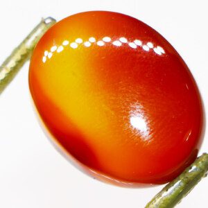 Closeup photo of a Sunset Agate loose gemstone held in tweezers, showcasing its orange, red, and purple hues.