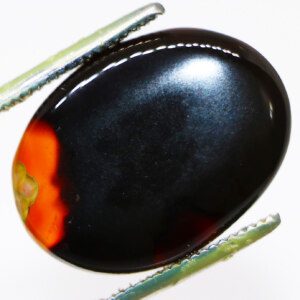 Close-up of black agate loose gemstone held in tweezers.