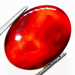 Close-up photo of a Natural Red Agate loose gemstone held in tweezers, showcasing its vibrant red color and unique patterns.