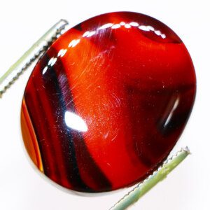 Closeup photo of a Red Striped Agate loose gemstone held in tweezers, showcasing its red and white bands.